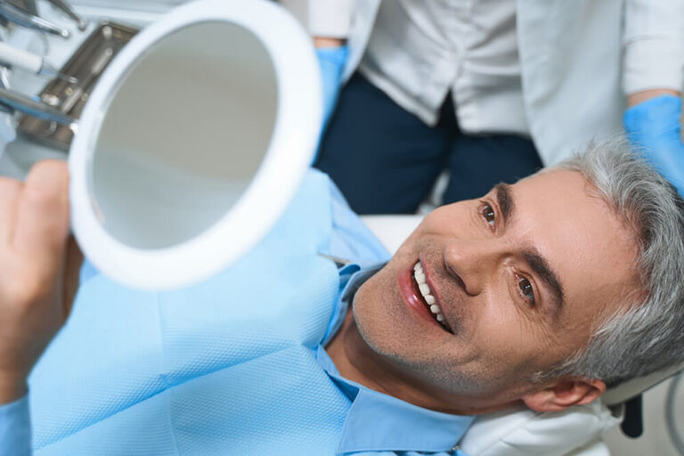 man smiling in mirror after getting veneers cosmetic dental procedures